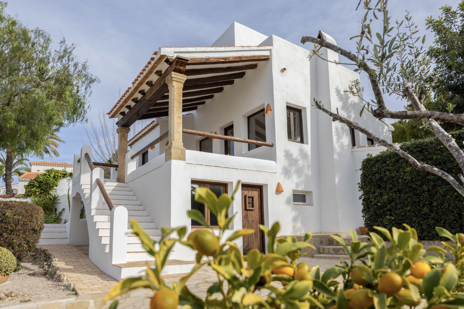Exterieur van de villa in Jávea, met de witte gevel, een overdekt terras met houten balken en een trap.
