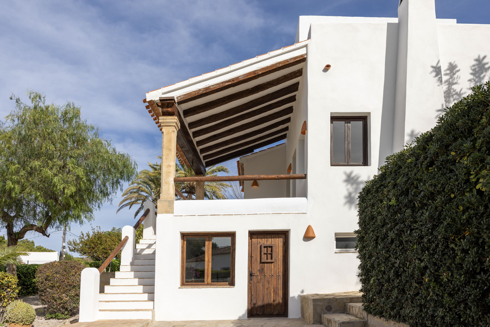Gevel van een mediterrane villa met een veranda met houten balken en een getrapte toegang tot de tuin.