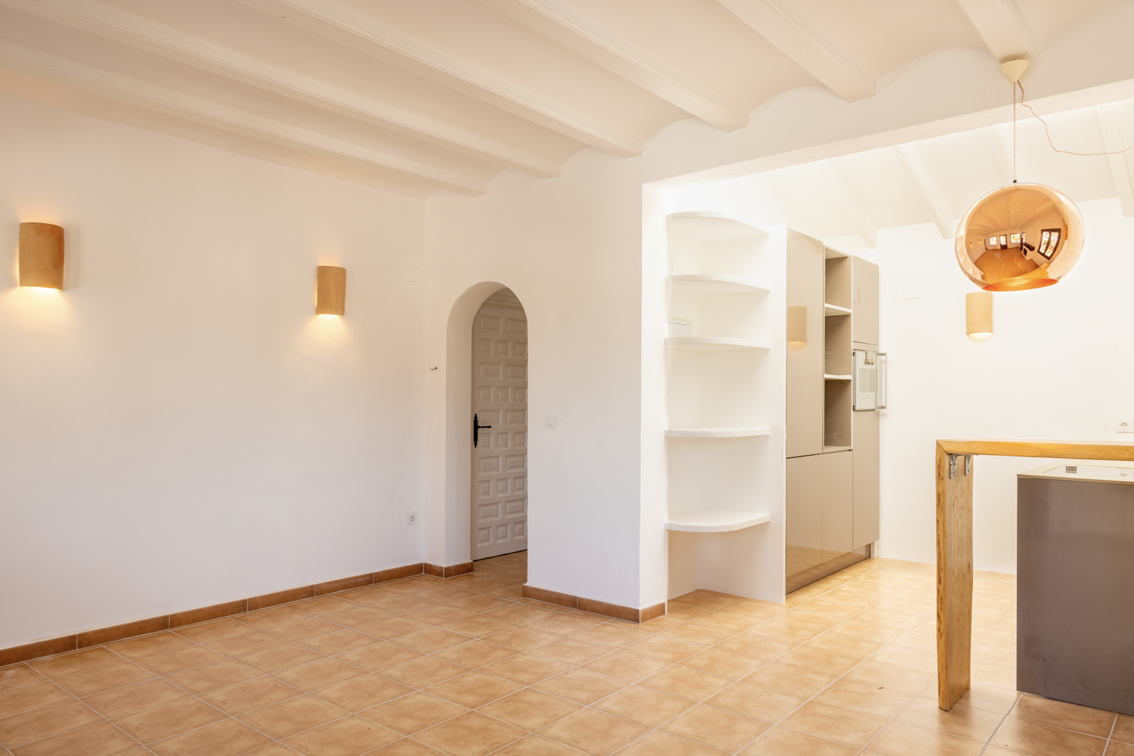 Licht interieur met witte schappen en een open keuken. Een koperkleurige bolvormige hanglamp hangt erboven.