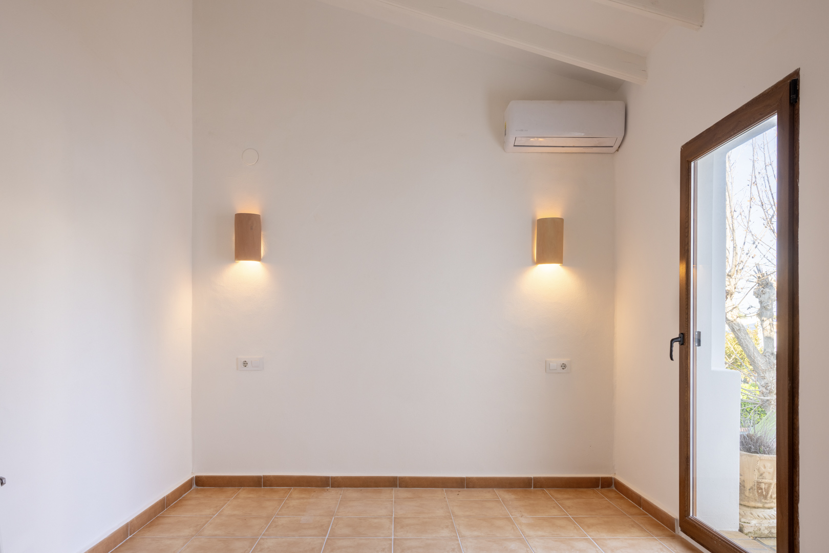 Lichte kamer met houten wandlampen en tegelvloer, met toegang naar buiten.