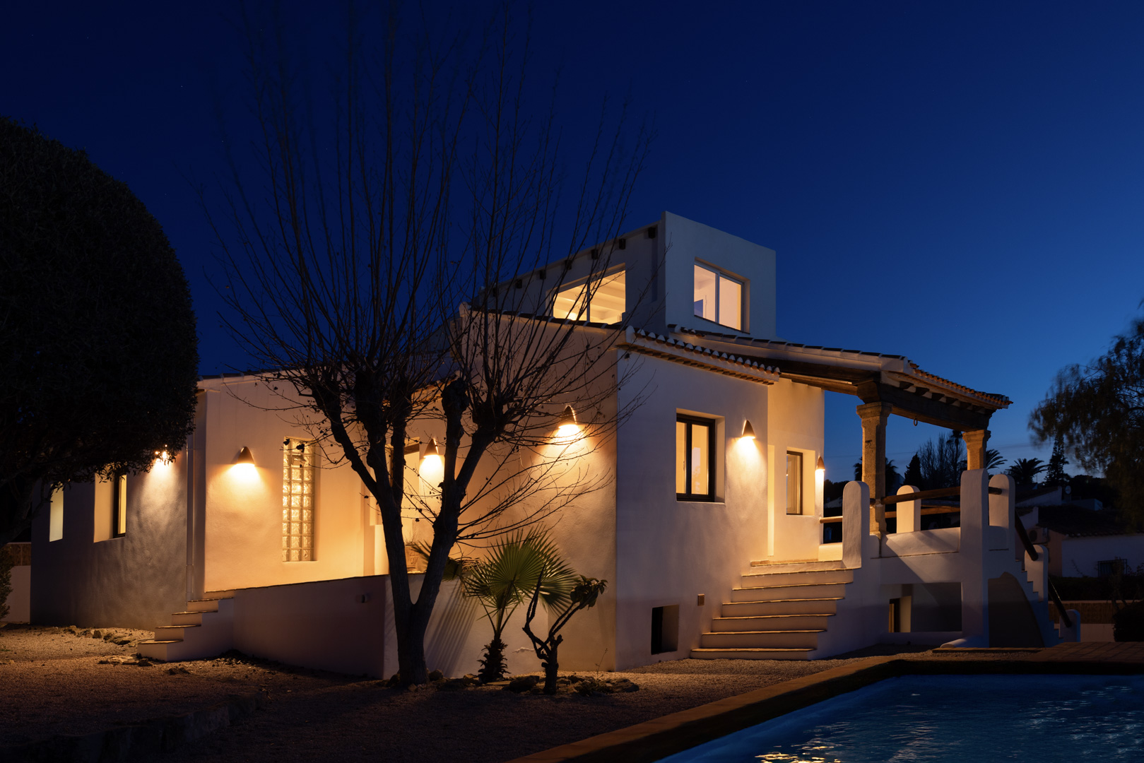 Nachtzicht van de verlichte villa met reflecterend zwembad en traditionele witte gevel.