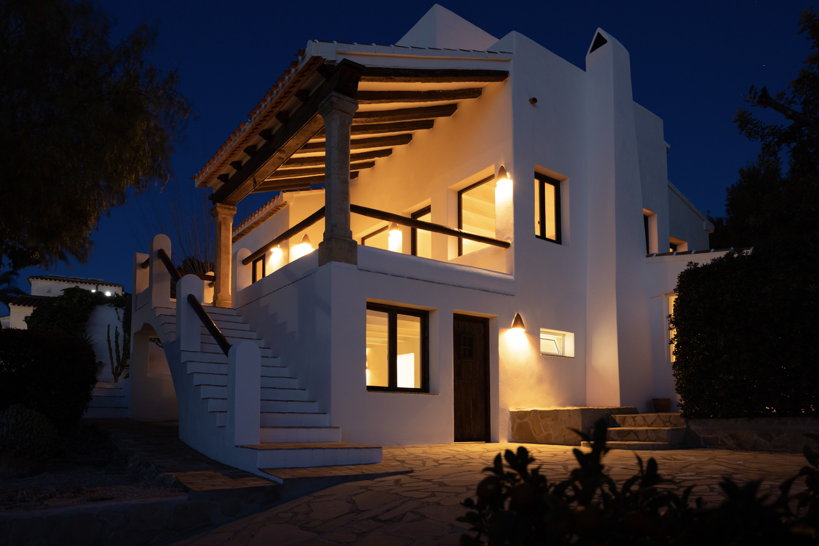 Nachtzicht van de villa met een verlicht, overdekt terras en stenen buitentrap.