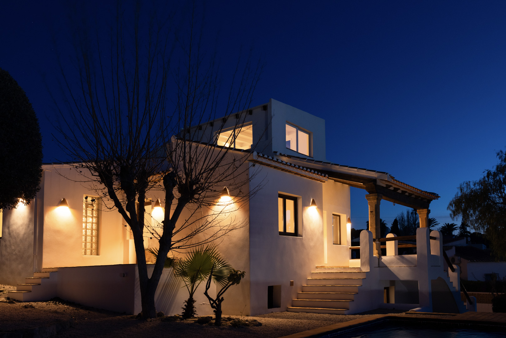 Nachtzicht van de villa met een verlichte witte gevel en stenen details op de veranda.