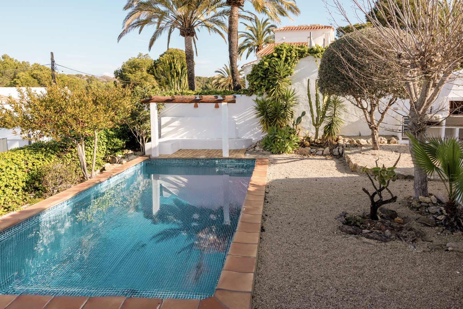 Rechthoekig zwembad met terracotta rand en pergola-overdekt solarium in een mediterrane tuin.