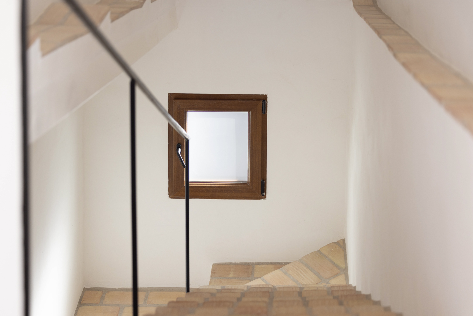 Trapdetail met zwarte leuning en houten raam in een witte muur.