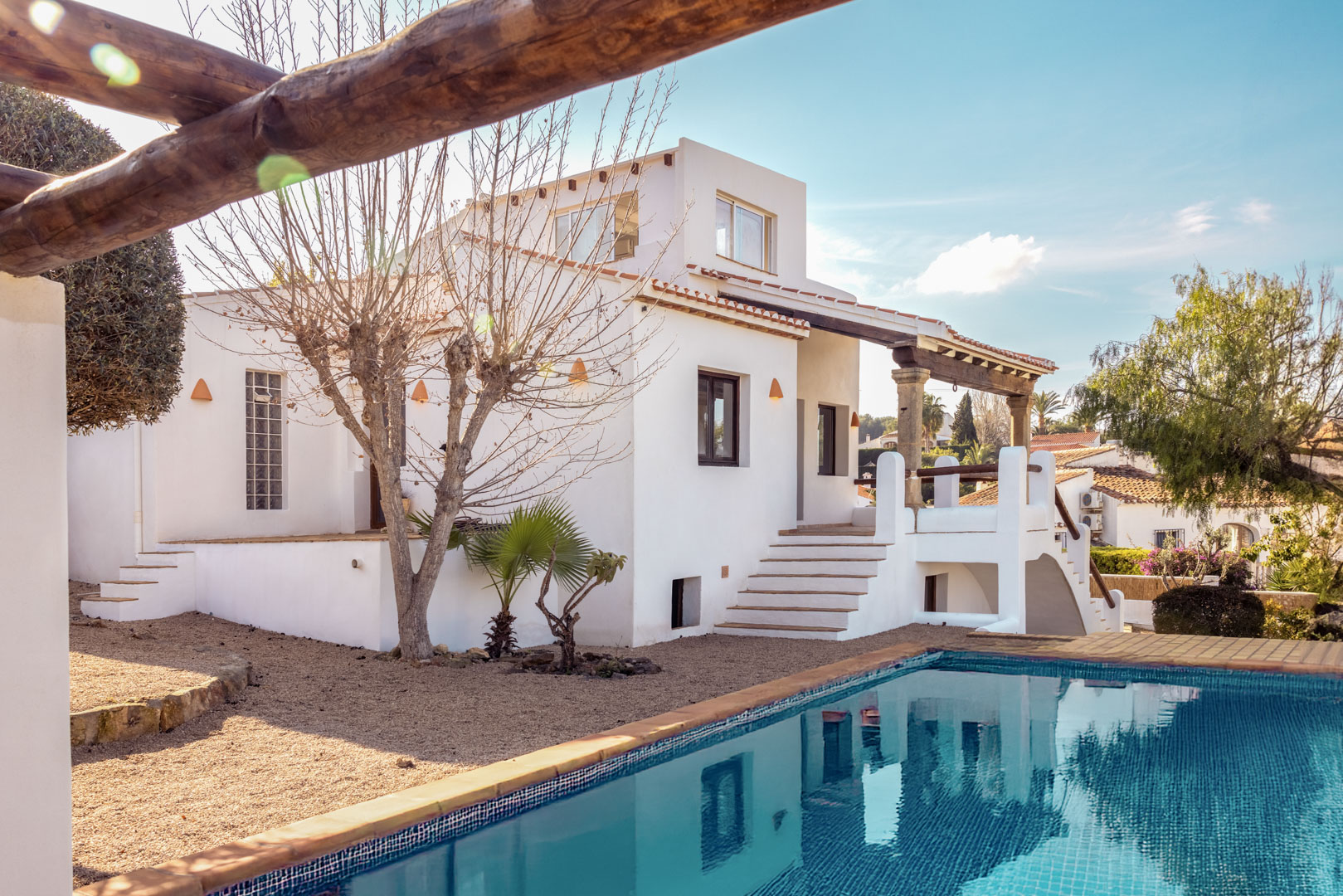 Uitzicht op de villa met turquoise blauw zwembad en witte gevel. Mediterraan design met grindtuin.