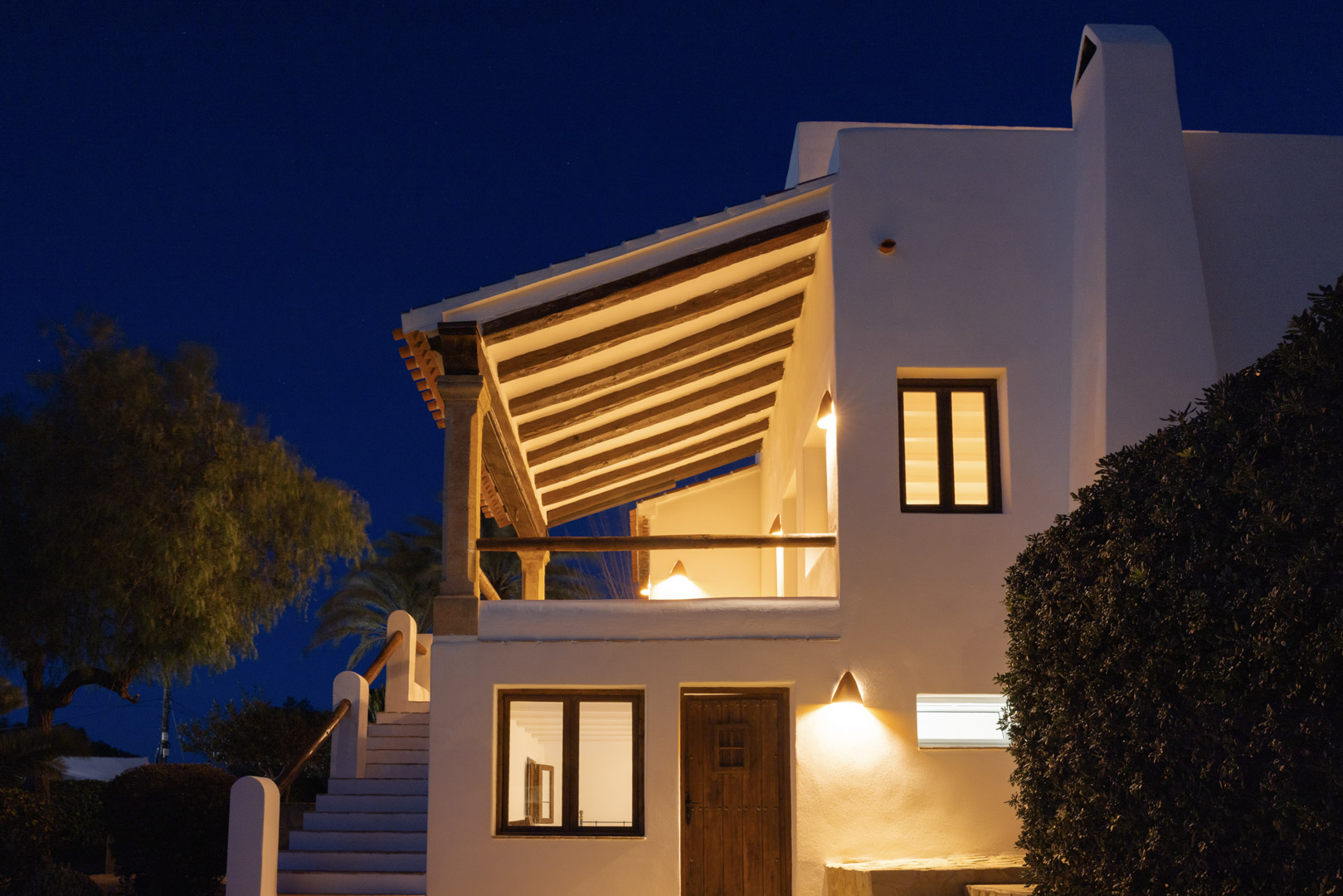 Verlichte villa-gevel in Tosalet, Jávea. Mediterrane architectuur met overdekt terras en houten details.