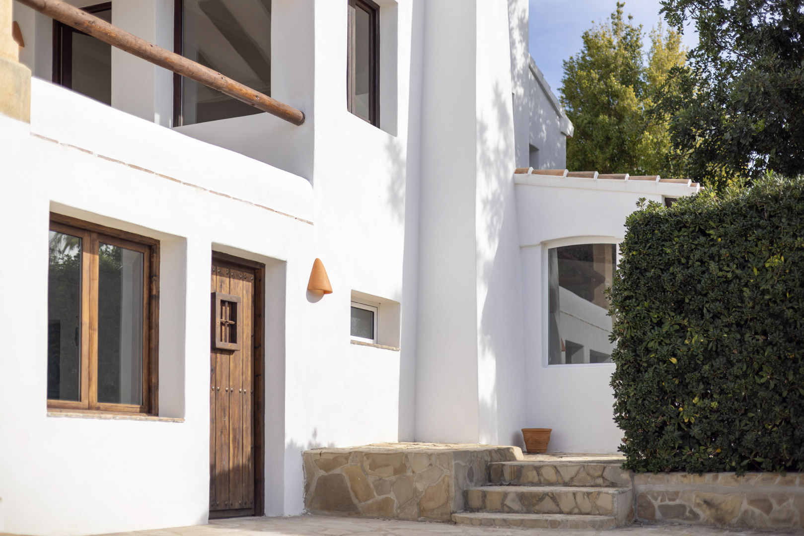 Villa-gevel in Jávea met rustieke details: houten deur, witte muren en stenen trappen.