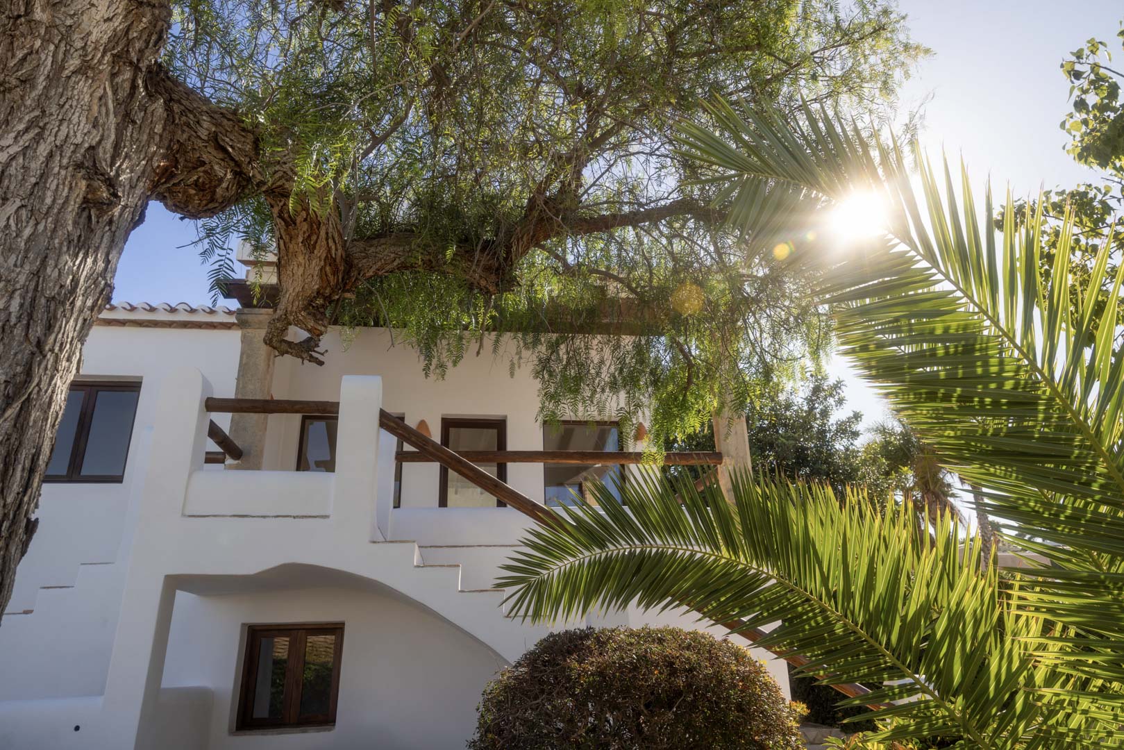Witte gevel met houten balkon en weelderig groen, dat de mediterrane architectuur benadrukt.