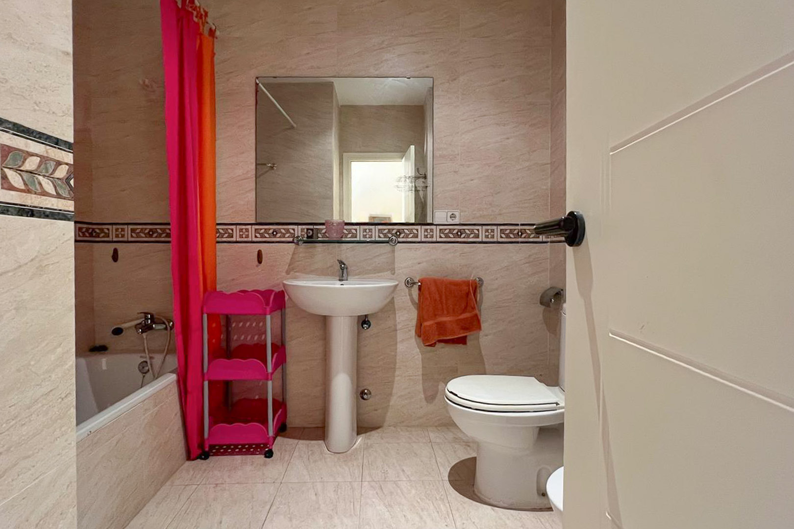 Badkamer met crèmekleurige tegels, een witte wastafel op voetstuk en decoratieve wanddetails.