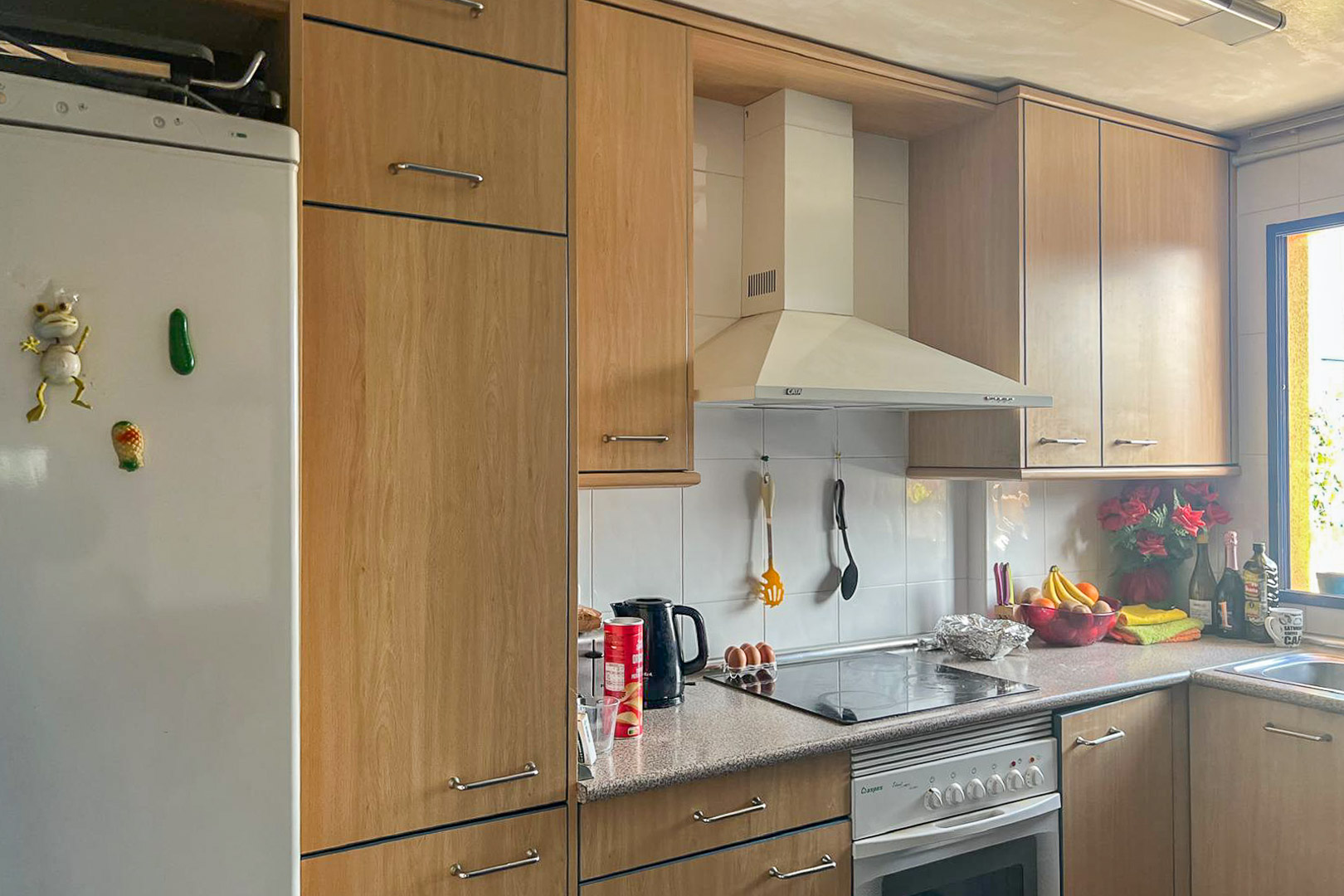 Functionele keuken met lichte houten kasten, witte apparaten en een granieten aanrecht.