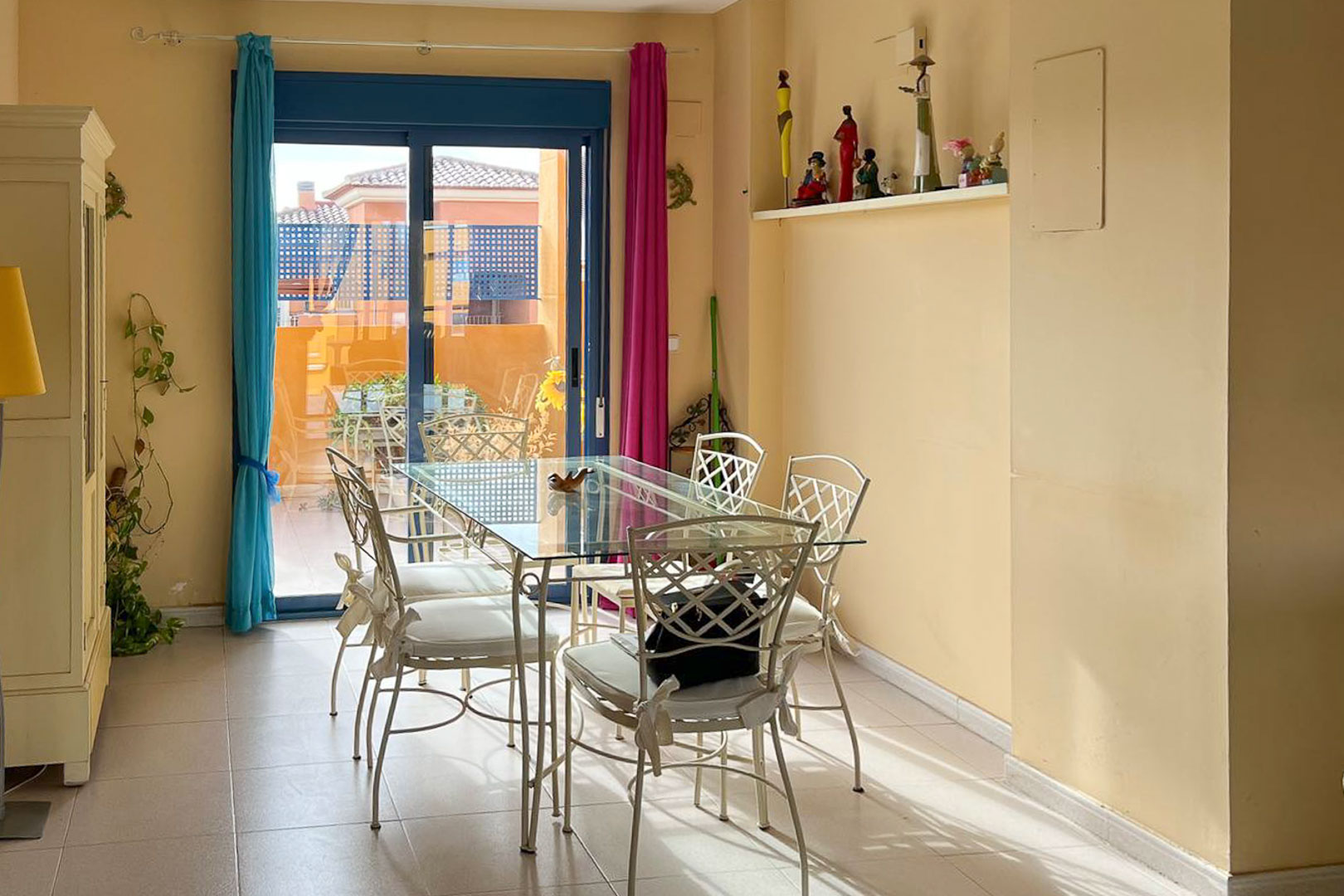 Lichte eetkamer met glazen tafel en smeedijzeren stoelen, toegang tot een terras met uitzicht.