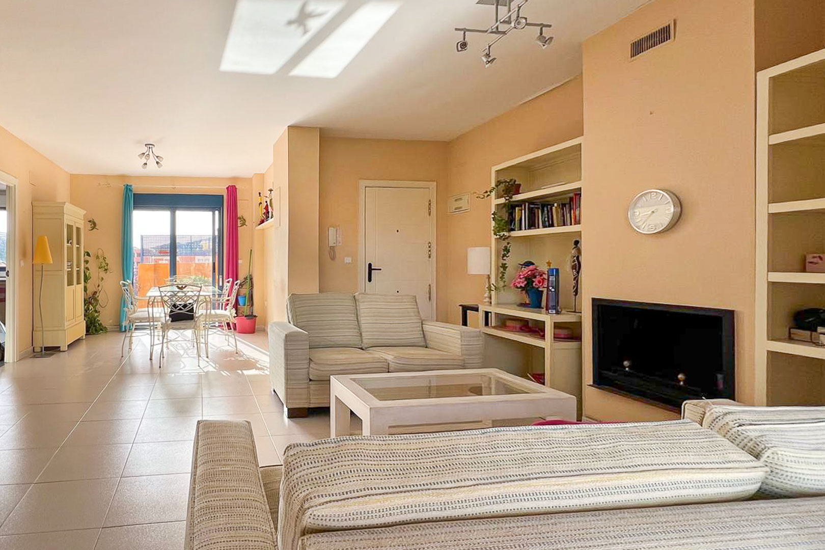 Lichte woonkamer met gestreepte banken, ingebouwde planken en toegang tot het terras.