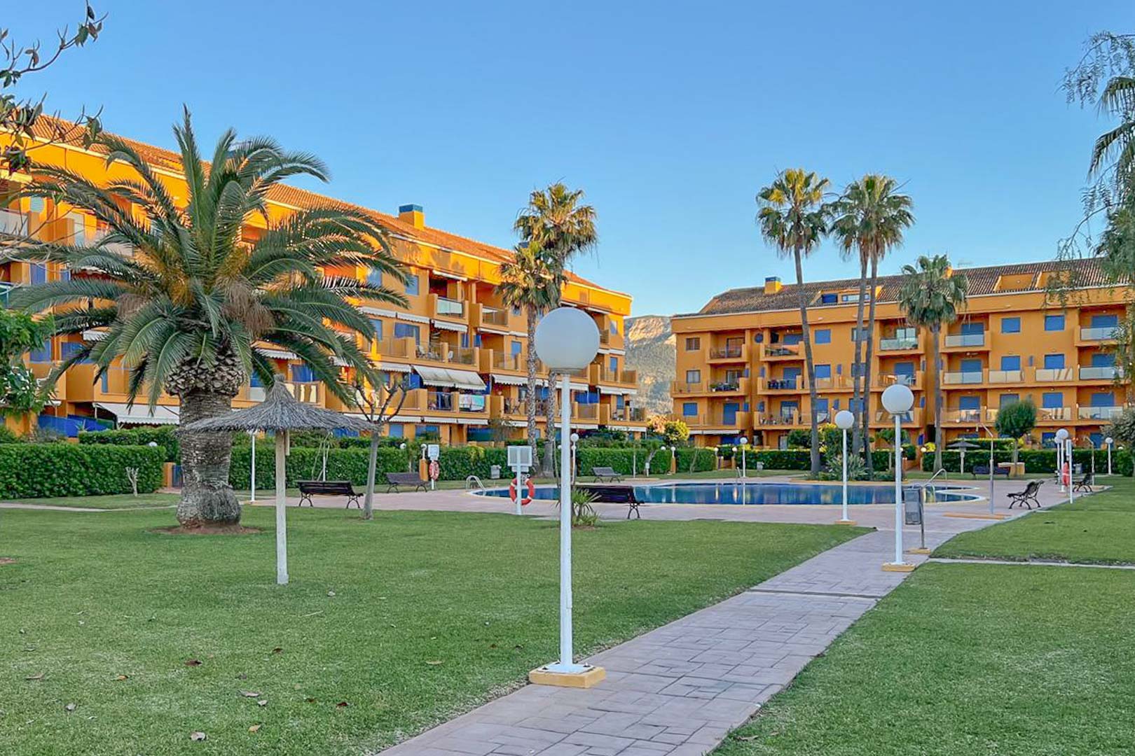 Uitzicht op de gemeenschappelijke tuin met zwembad, palmbomen en woongebouwen in Dénia.