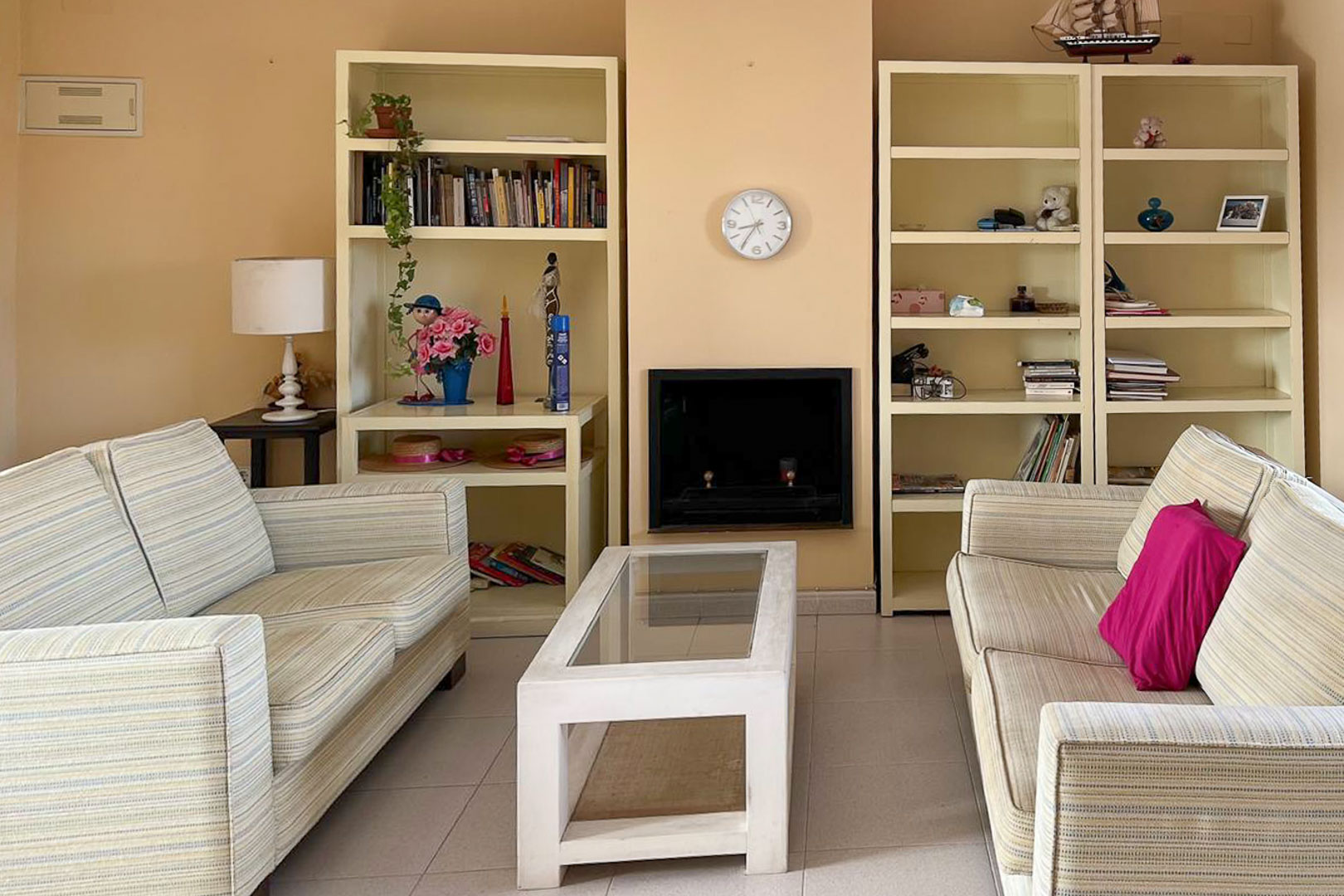 Woonkamer met gestreepte banken, ingebouwde stellingkasten en decoratieve open haard.