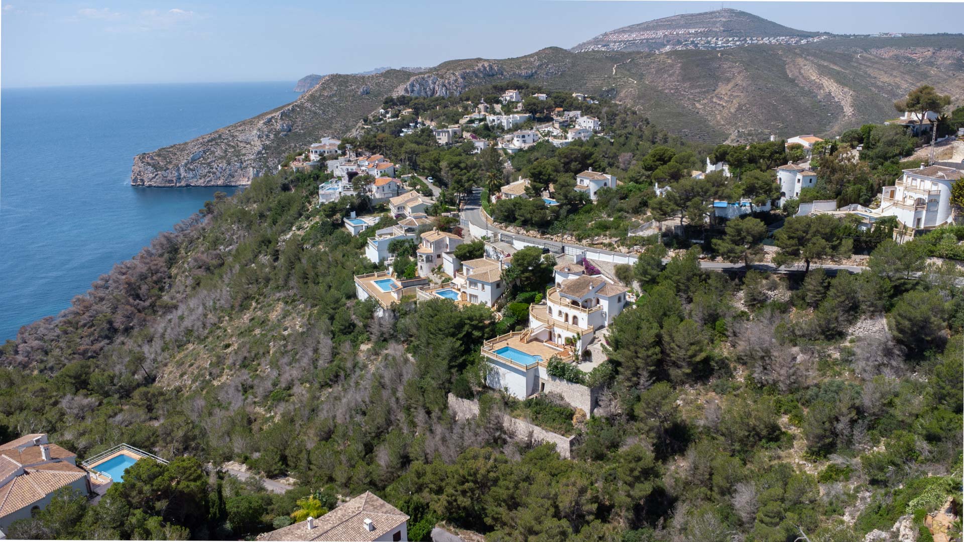 Luchtfoto van de kustlijn van Jávea met residentiële villa's op een beboste heuvel met uitzicht op de Middellandse Zee en de kliffen.