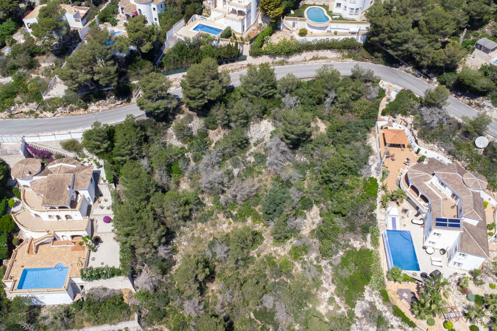 Luchtfoto van het hellende perceel met mediterrane vegetatie, gelegen tussen bestaande villa's met privézwembaden in de wijk Costa Nova.
