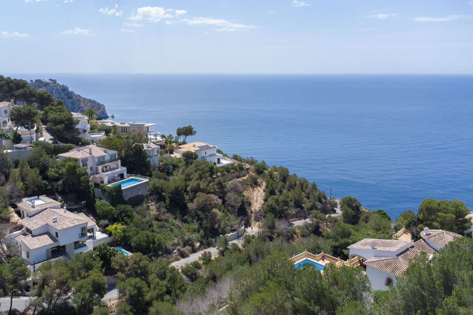 Verhoogd uitzicht op de kustlijn van Jávea met mediterrane villa's tussen de pijnbomen en een weids uitzicht over de diepblauwe Middellandse Zee.