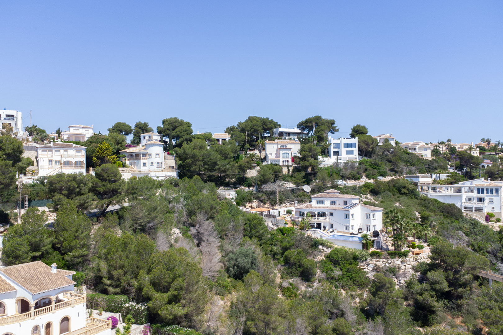Verhoogd uitzicht op de woonwijk Costa Nova in Jávea, met mediterrane villa's gelegen op een beboste heuvel onder een helderblauwe lucht.