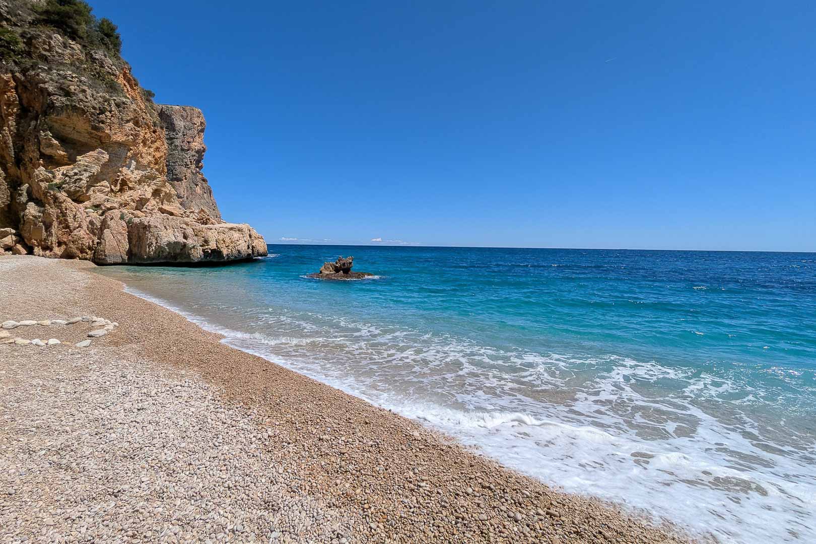 Cala Llebeig, een afgelegen kiezelbaai met turquoise water en kalkstenen kliffen, direct toegankelijk vanuit de wijk La Arnella in Moraira.