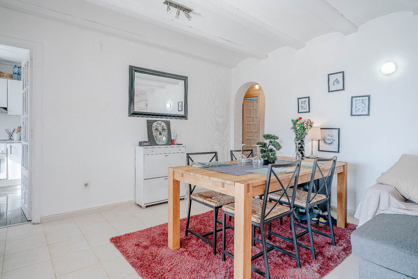 Eethoek met een houten tafel en metalen stoelen op een rood tapijt, voorzien van witte balkenplafonds en een karakteristieke boogdoorgang.