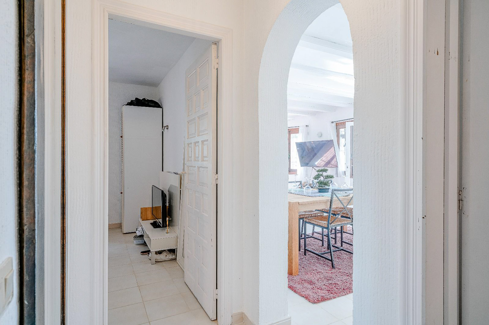 Hal met een mediterrane boog die leidt naar de eetkamer en een witte paneeldeur die toegang geeft tot een lichte slaapkamer.