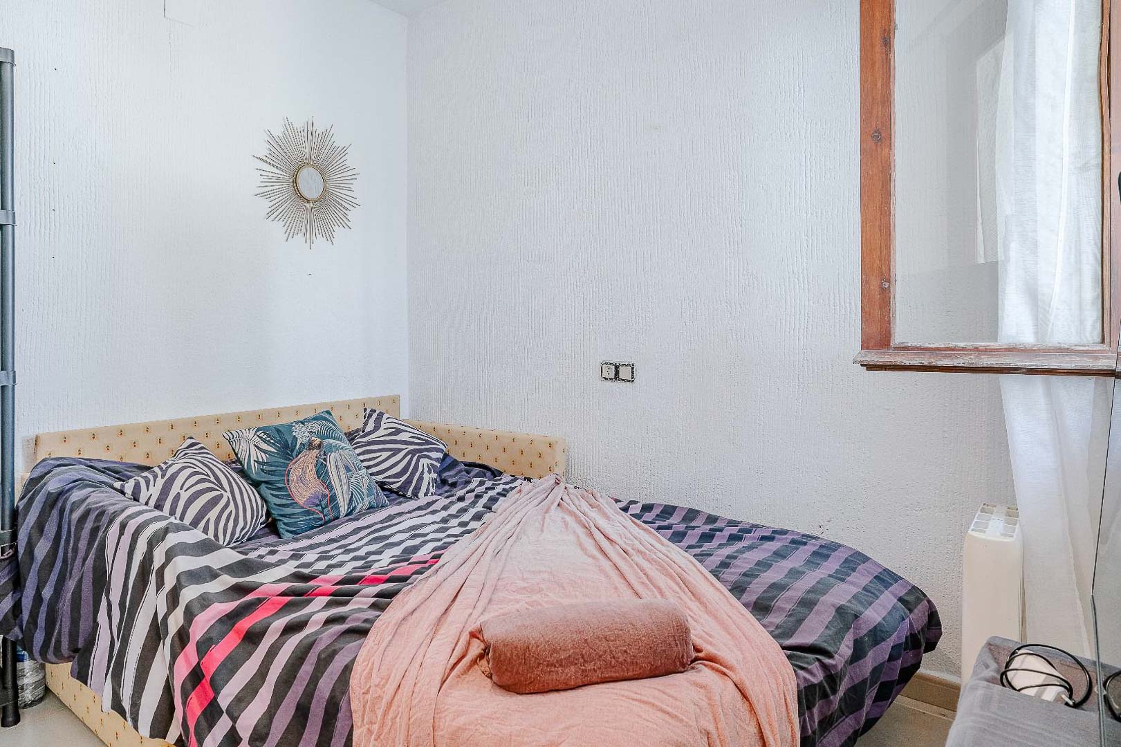 Lichte slaapkamer met muren met textuur, een eenpersoonsbed met gestoffeerd hoofdbord en een houten raamkozijn voor natuurlijk licht.
