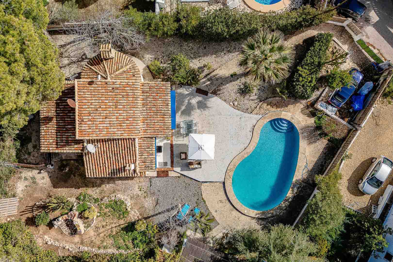 Luchtfoto van de villa met niervormig zwembad, verhard terras en traditioneel pannendak op een ruim perceel met mediterrane beplanting.