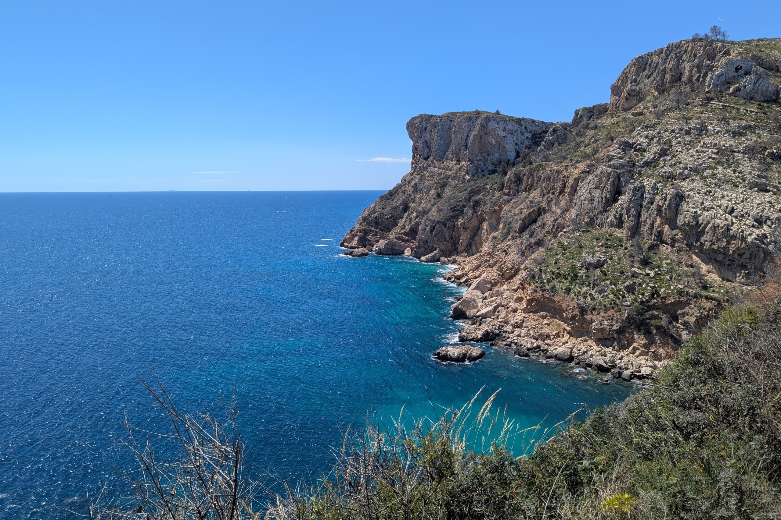 Panoramisch uitzicht op de ruige kalksteenkliffen en het turquoise mediterrane water nabij Cala Llebeig, omgeven door inheemse kustvegetatie.