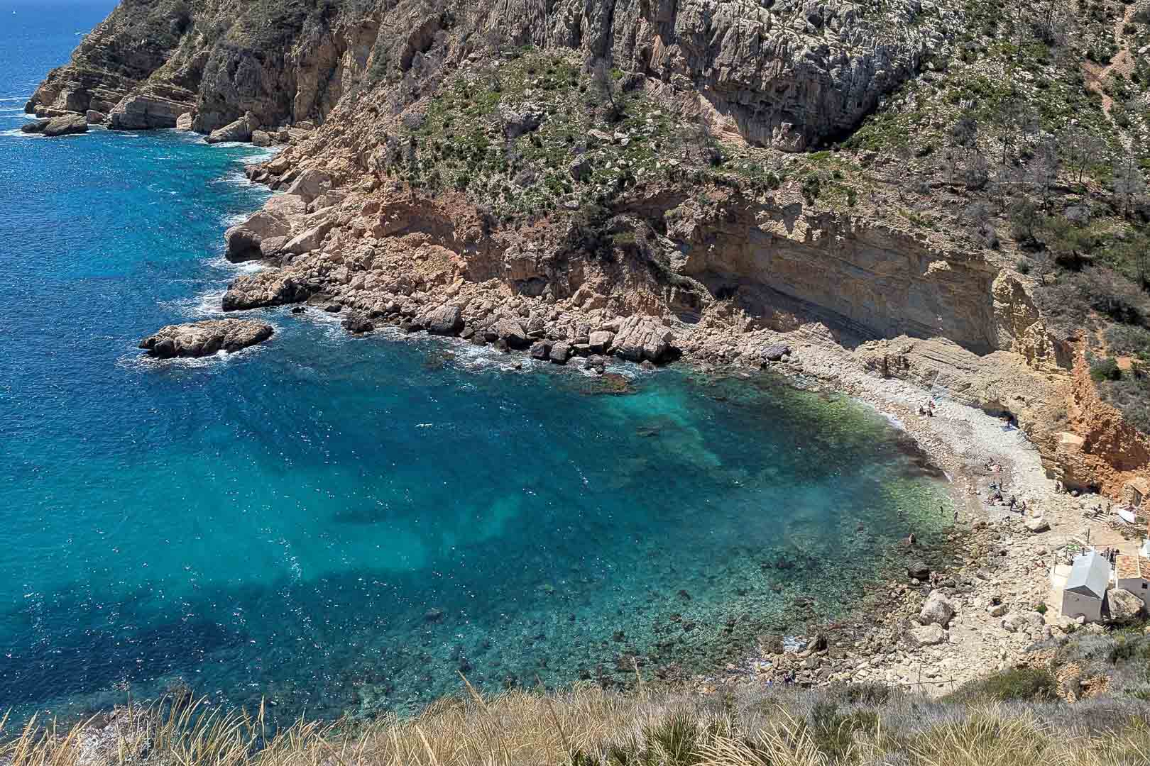 Uitzicht op Cala Llebeig met kristalhelder turquoise water en steile kliffen, bereikbaar via een pad nabij de achterzijde van het perceel.