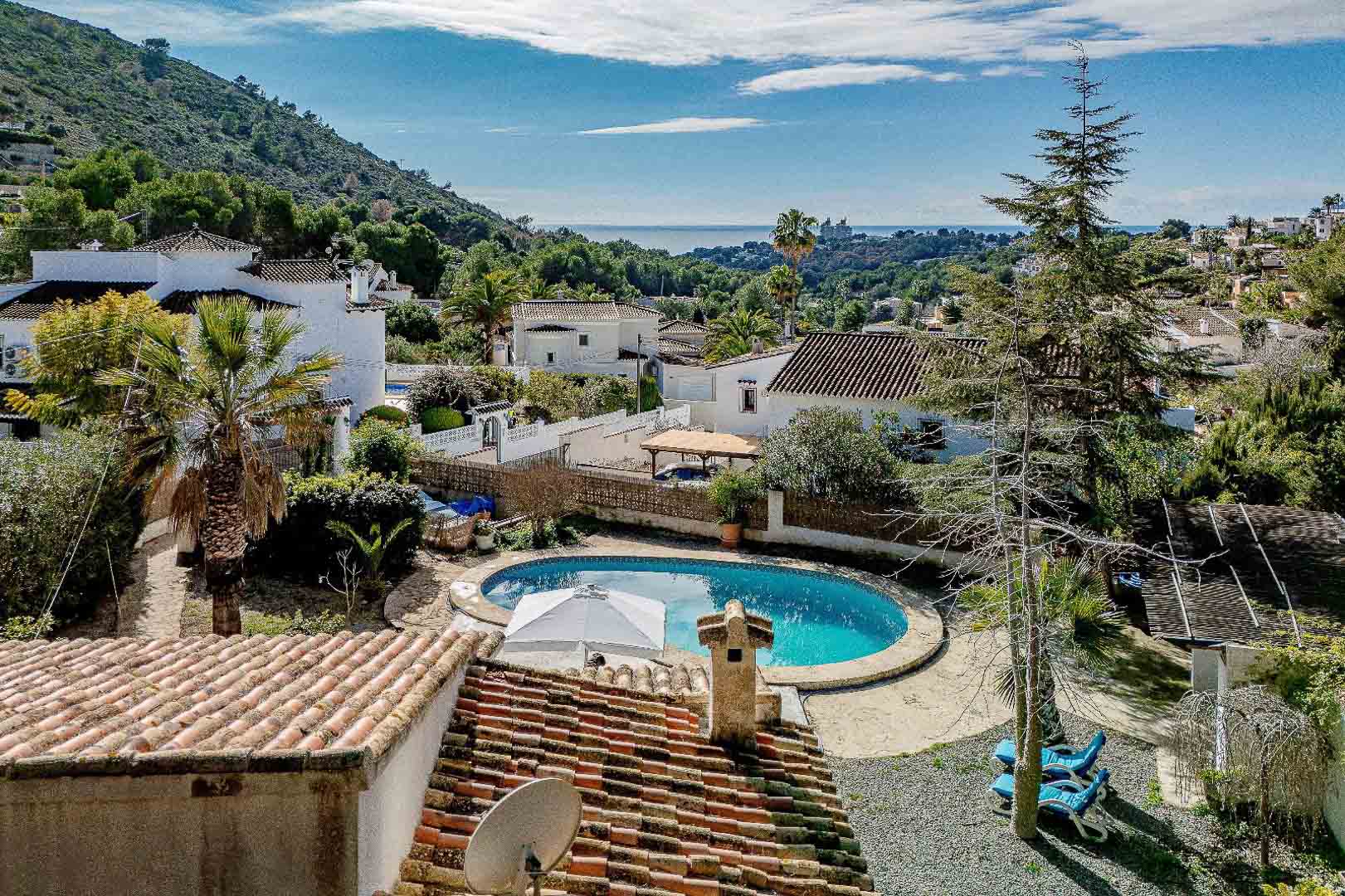 Verhoogd zicht op het niervormige privézwembad en de mediterrane tuin, met panoramisch uitzicht op zee en de omliggende woonwijk van Moraira.