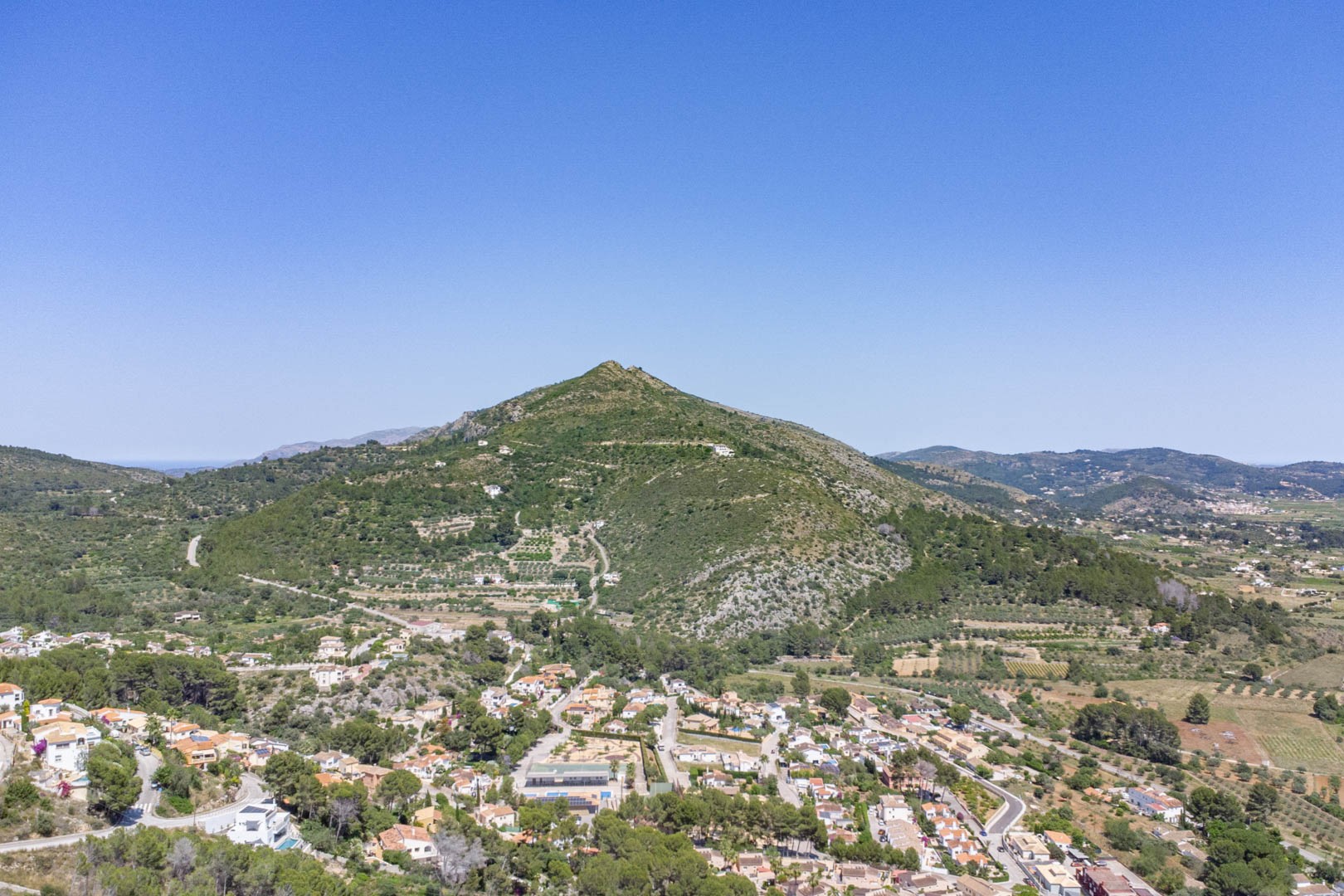 Panoramisch luchtfoto van de Jalón-vallei en het dorp Alcalalí, met uitzicht op het mediterrane berglandschap en de verspreide bebouwing in een groene omgeving.