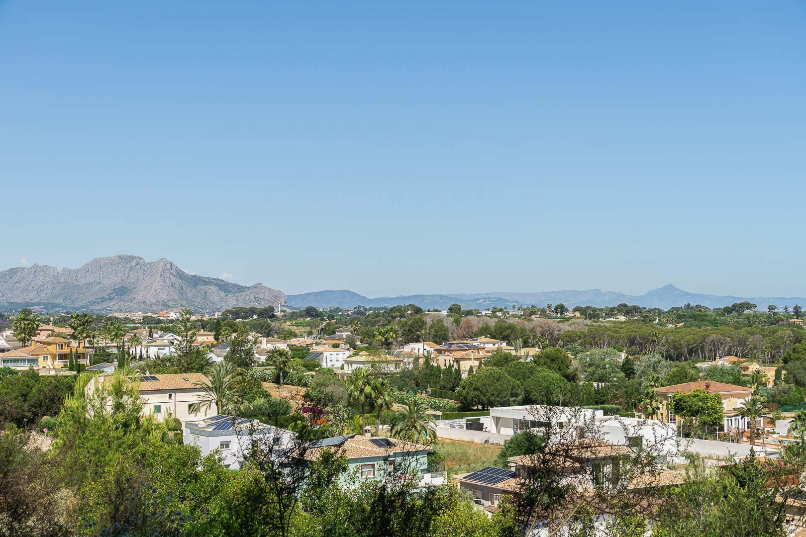 Panoramisch uitzicht op Dénia met huizen, groen en bergen op de achtergrond.