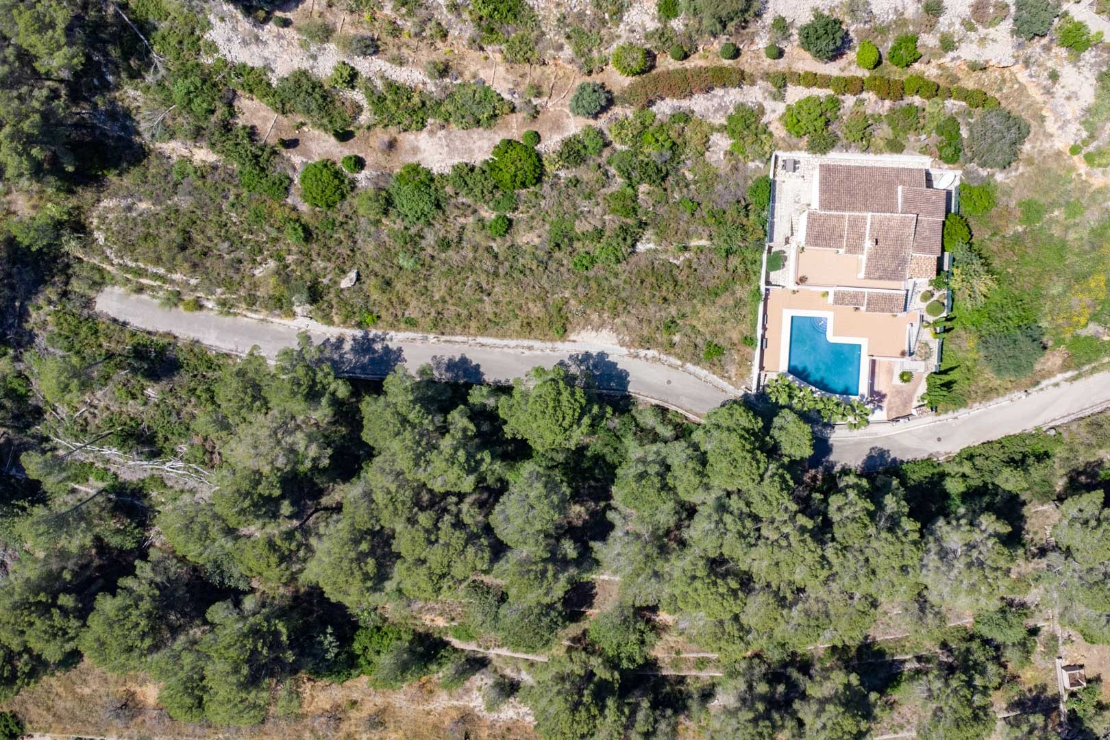Luchtfoto van een vrijstaande villa met privézwembad, omgeven door een dicht mediterraan boslandschap en een eigen toegangsweg.