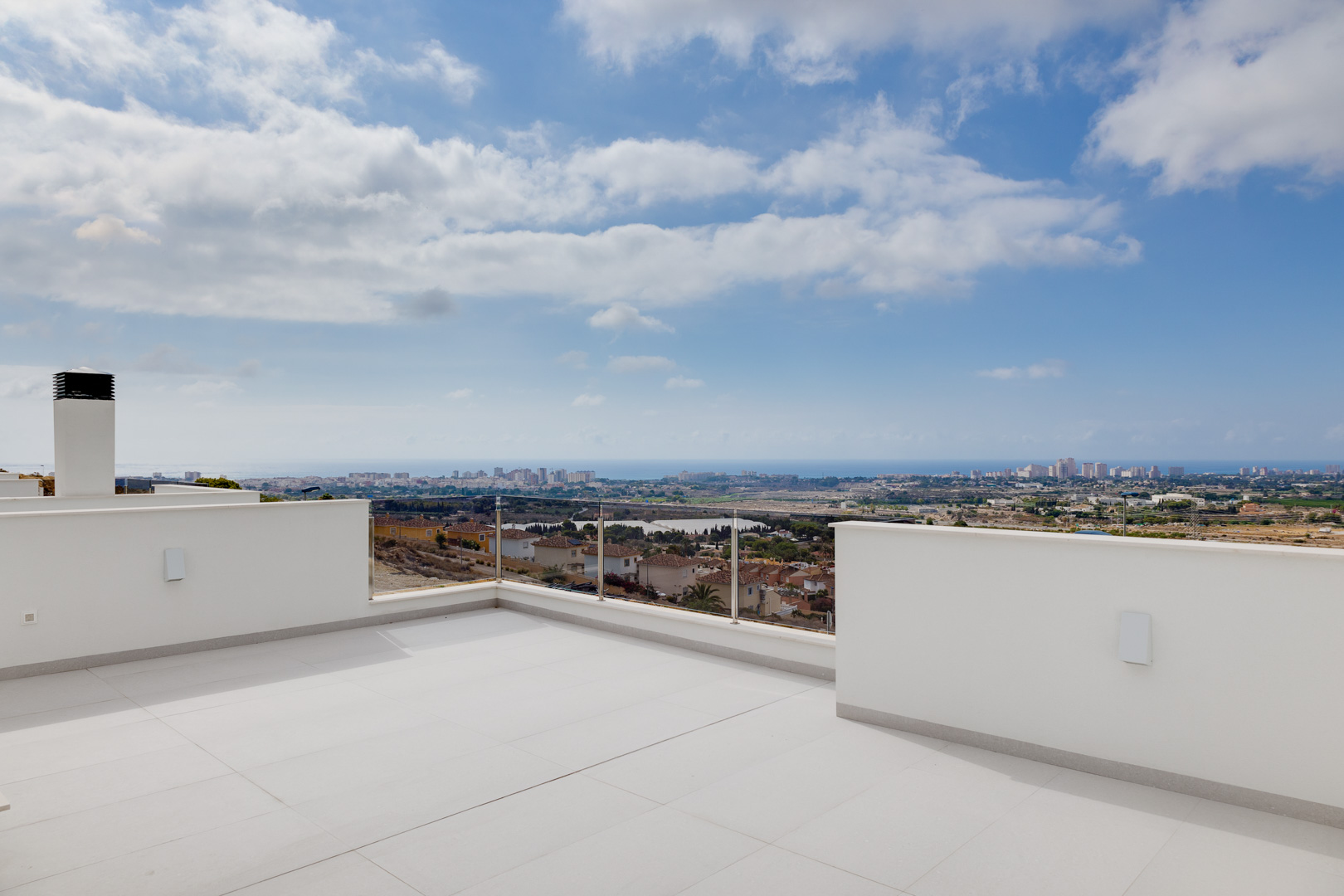 Bovenste terras met grootformaat keramische tegels, glazen balustrades en weids panoramisch uitzicht over de kustlijn en de Middellandse Zee.