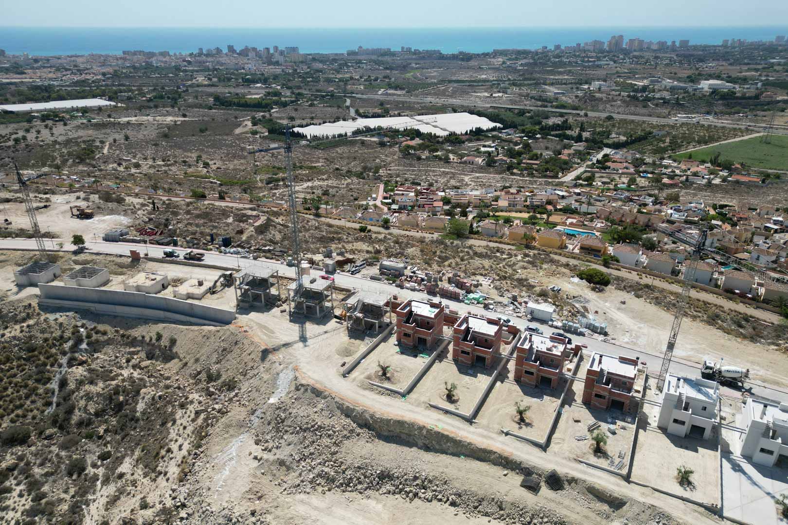 Luchtfoto van de villa's in aanbouw op een heuvel, met een panoramisch uitzicht over de Middellandse Zee en de omliggende kustlijn.