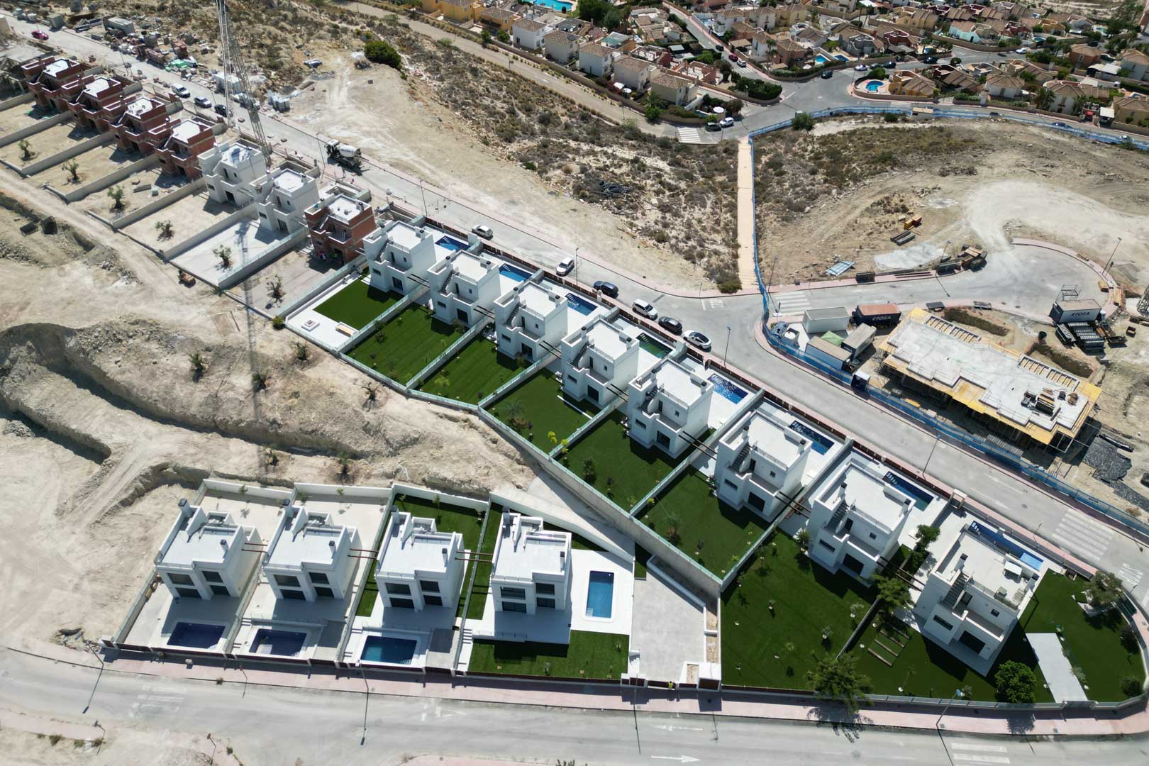 Luchtfoto van een nieuwbouwproject met moderne witte villa's, privézwembaden en tuinen, gelegen op een verhoogd perceel.