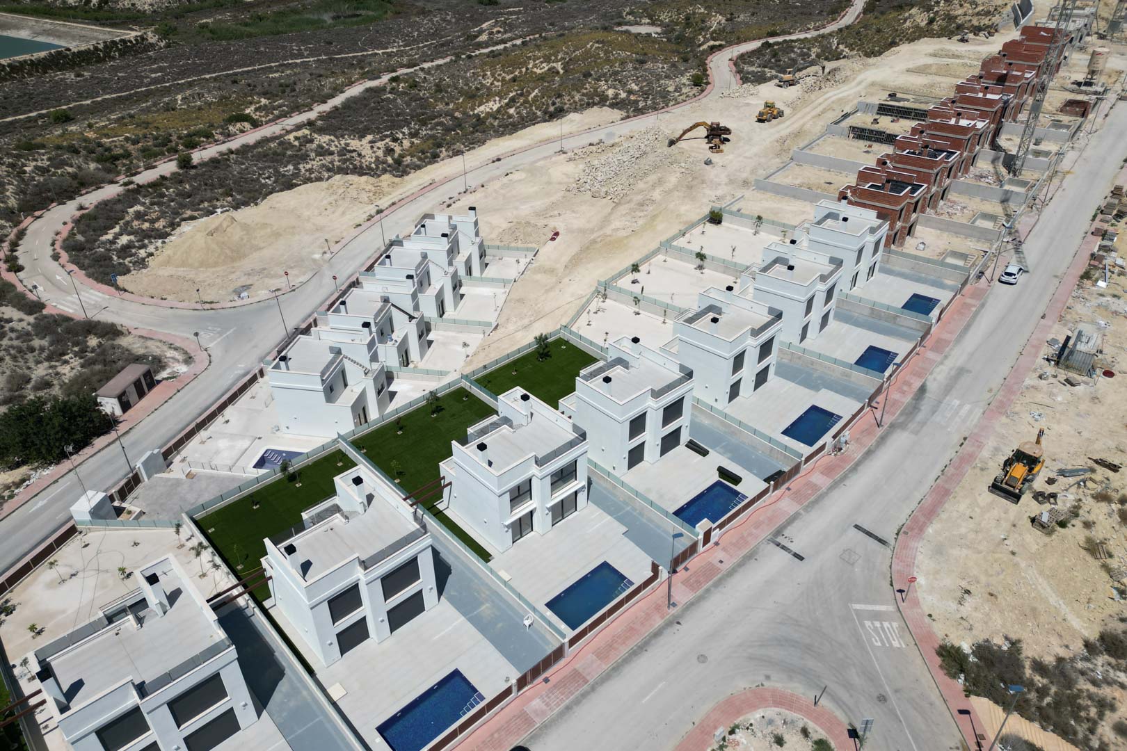 Luchtfoto van het nieuwbouwproject met witte kubistische villa's, elk met een privézwembad en terras, gelegen op een verhoogde locatie in ontwikkeling.