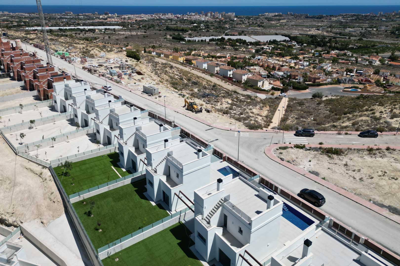 Luchtfoto van moderne villa's met privétuinen, zwembaden en dakterrassen, gelegen op een heuvel met panoramisch uitzicht over de kustlijn en de Middellandse Zee.