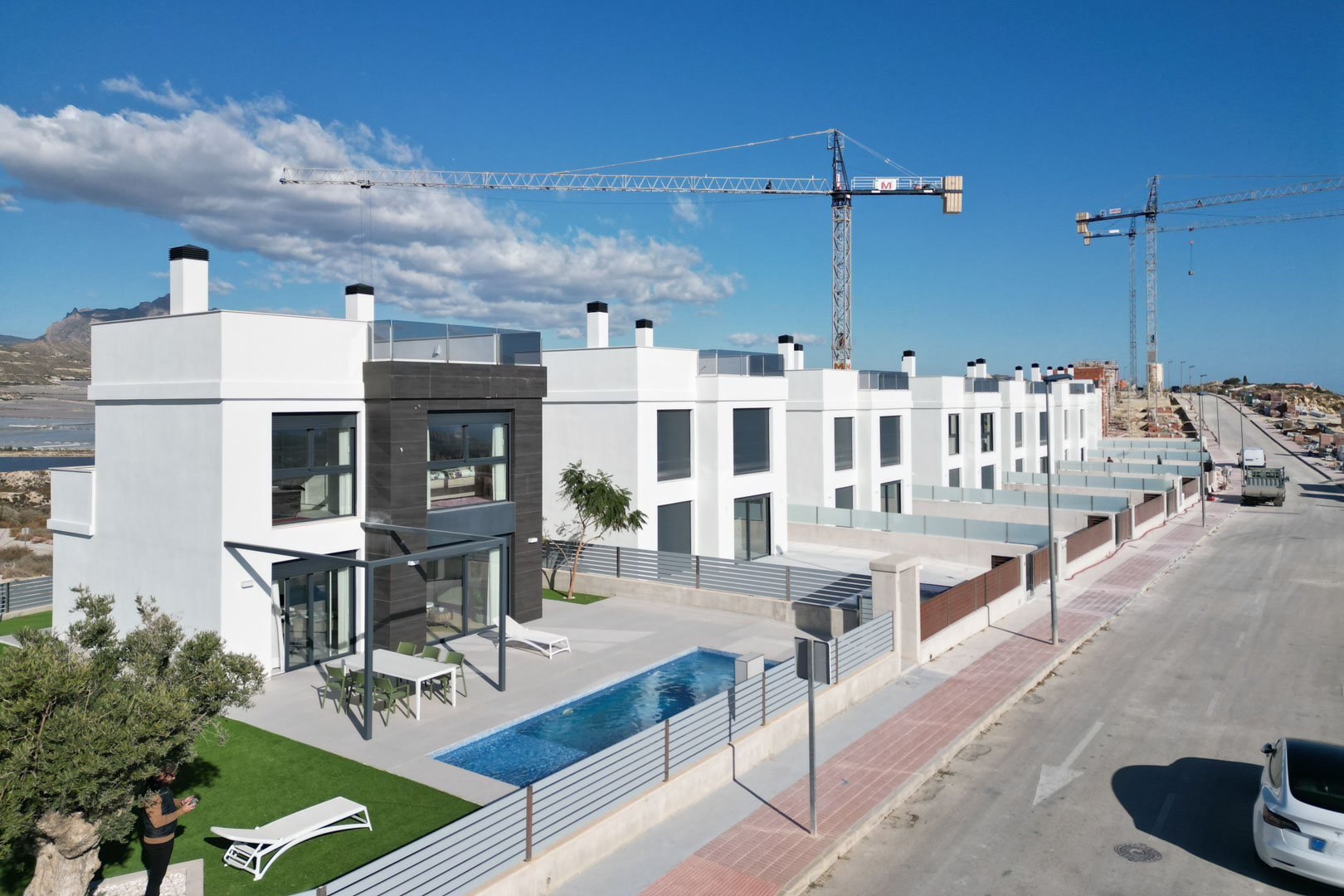 Luchtfoto van moderne villa's met witte gevels, donkere steenaccenten, privézwembaden, ingerichte terrassen en dakterrassen op een verhoogde locatie.