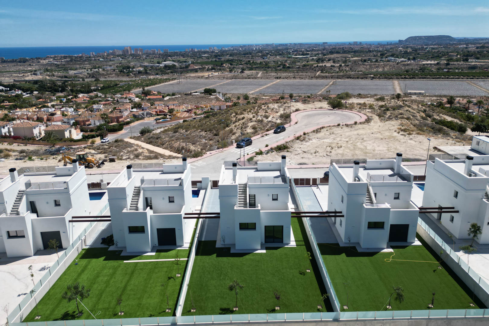 Luchtfoto van moderne witte villa's met privétuinen en dakterrassen, gelegen op een verhoogde positie met panoramisch uitzicht op de kustlijn en de zee.
