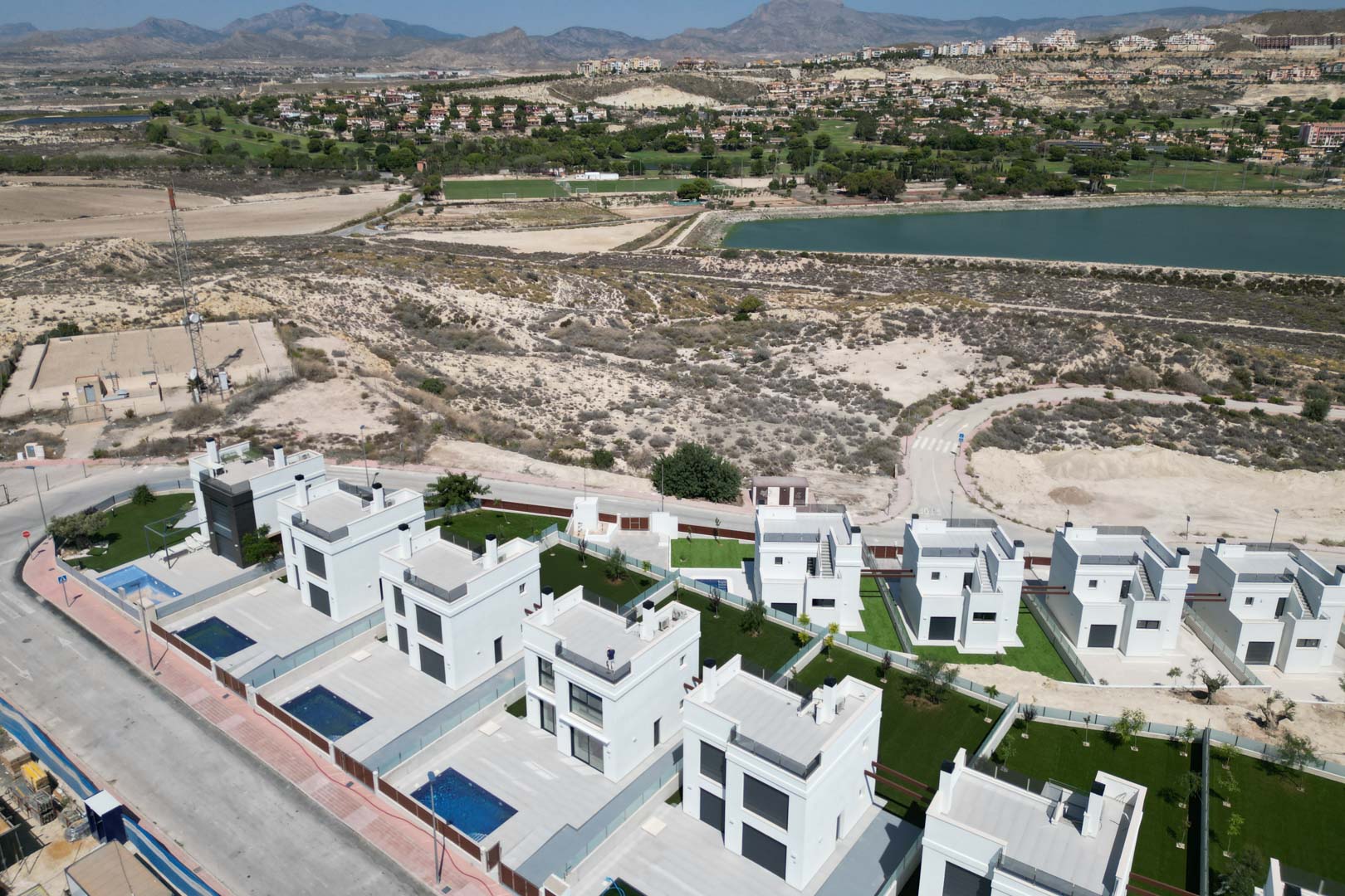 Luchtfoto van moderne witte villa's met privézwembaden en tuinen, gelegen nabij een golfbaan en reservoir met uitzicht op de bergen.