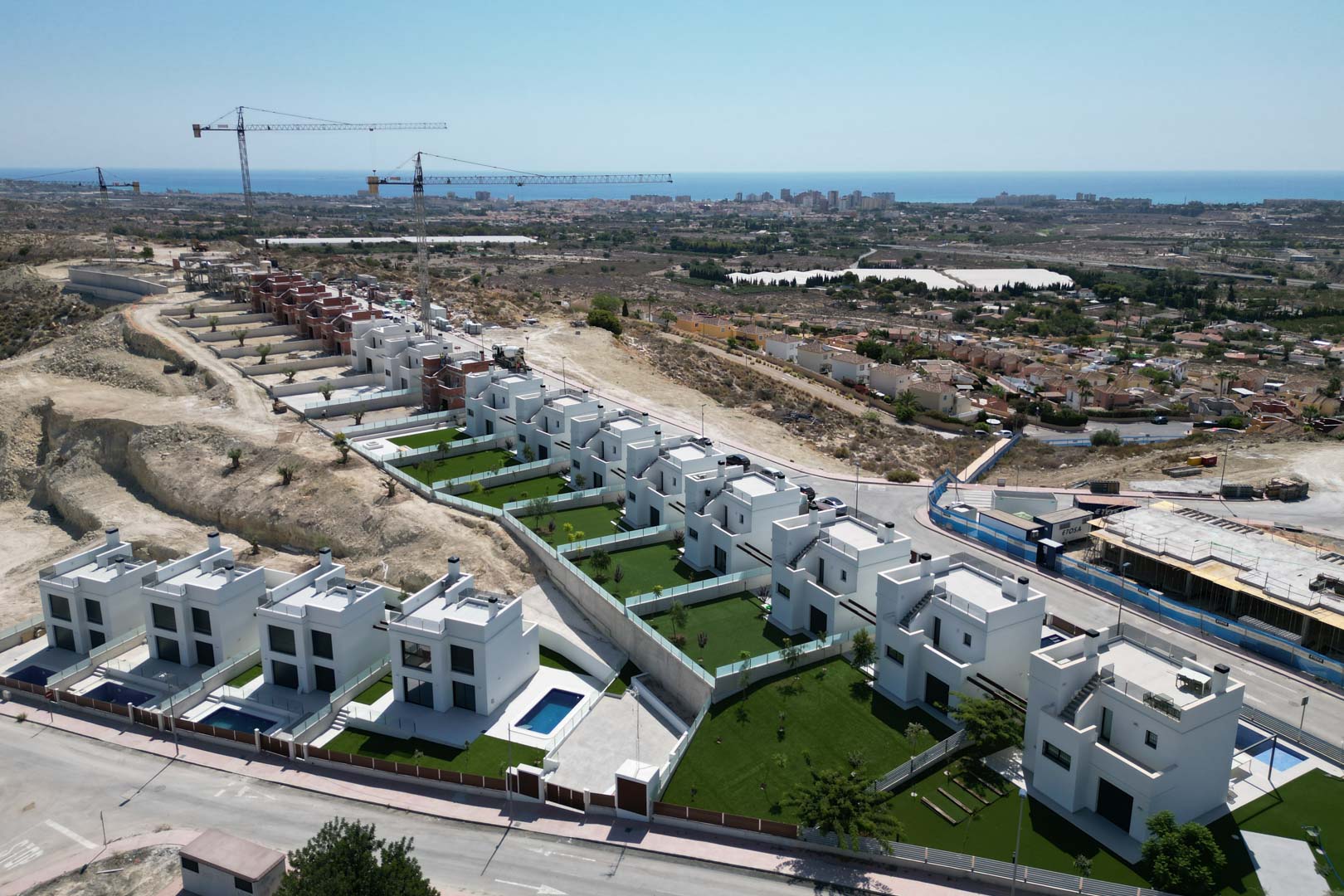 Luchtfoto van moderne witte villa's op een heuvel, met privétuinen, individuele zwembaden en een verhoogd uitzicht over de Middellandse Zeekust.