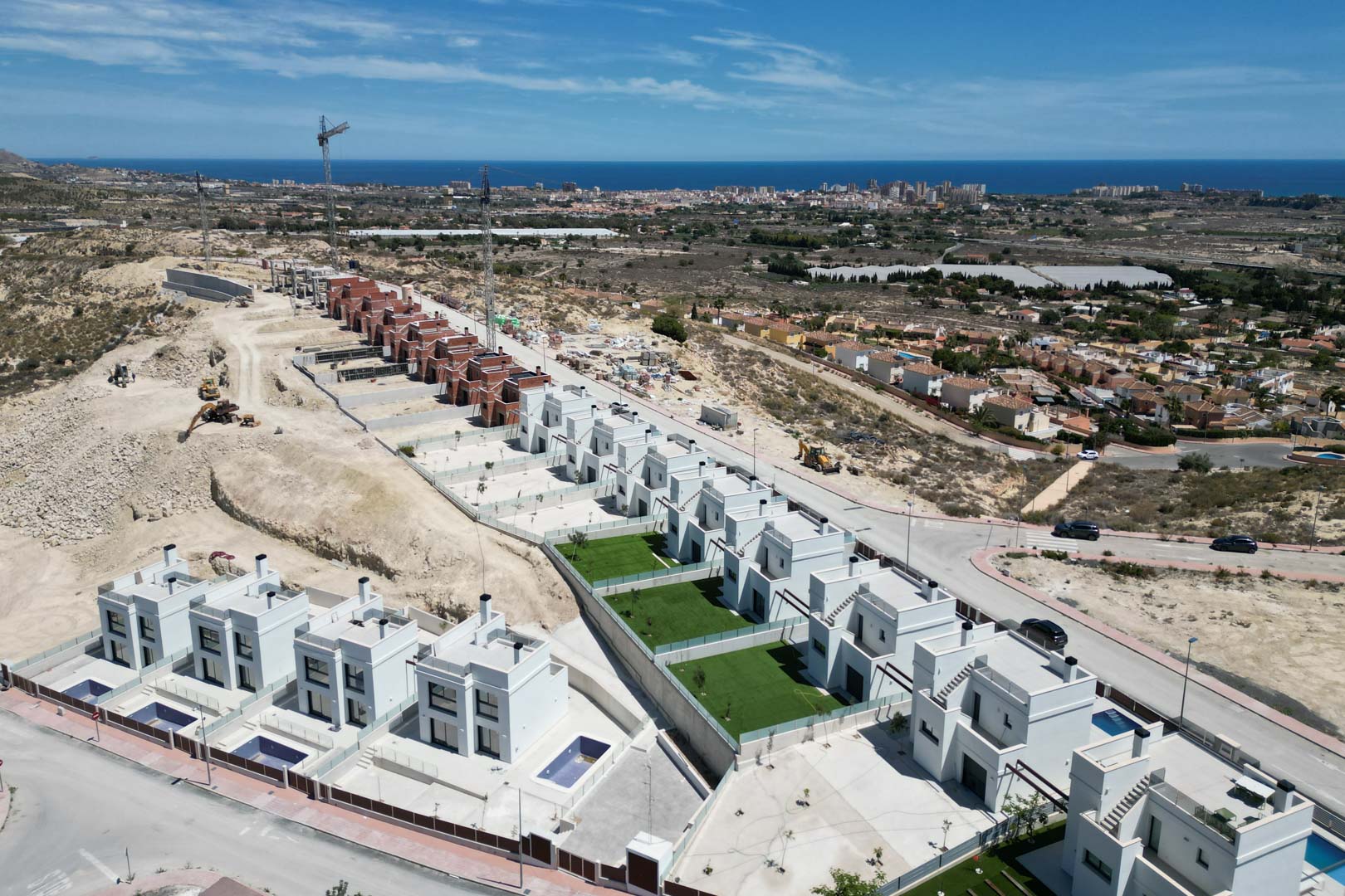 Luchtfoto van moderne witte villa's op een heuvel, voorzien van privézwembaden en tuinen met panoramisch uitzicht op de Middellandse Zee en de kustlijn.