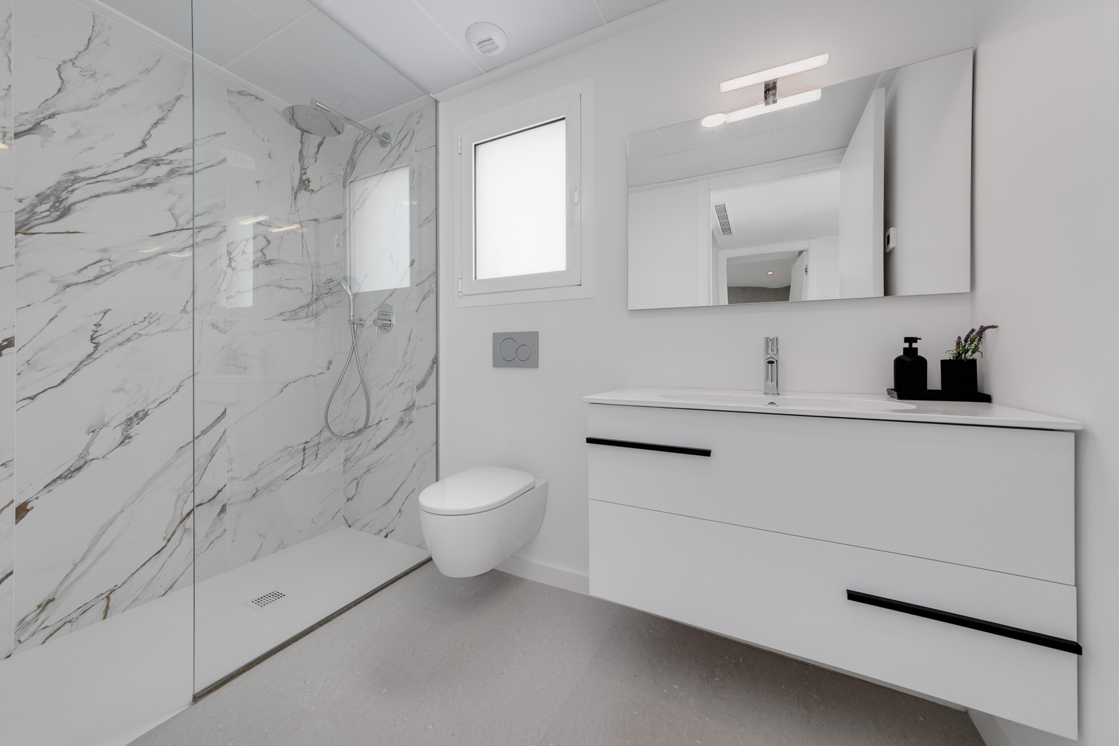 Moderne badkamer met inloopdouche afgewerkt met marmerlook porselein, hangend toilet en zwevend wastafelmeubel met zwarte details.
