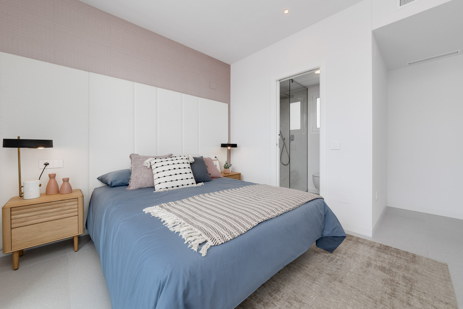 Moderne slaapkamer met wit gepaneeld hoofdbord, mauve accentmuur en een aangrenzende badkamer met glazen wand.