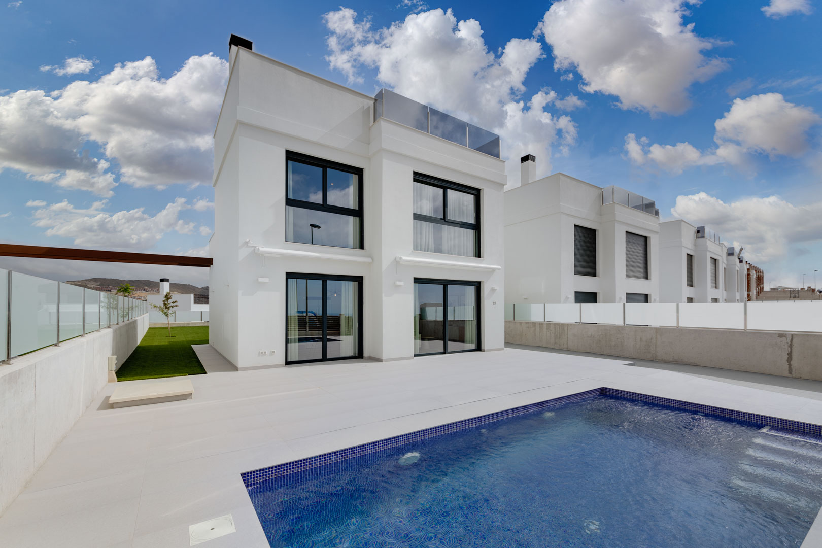 Moderne witte villa met zwarte raamkozijnen, een ruim betegeld terras en een privézwembad met blauwe mozaïektegels.