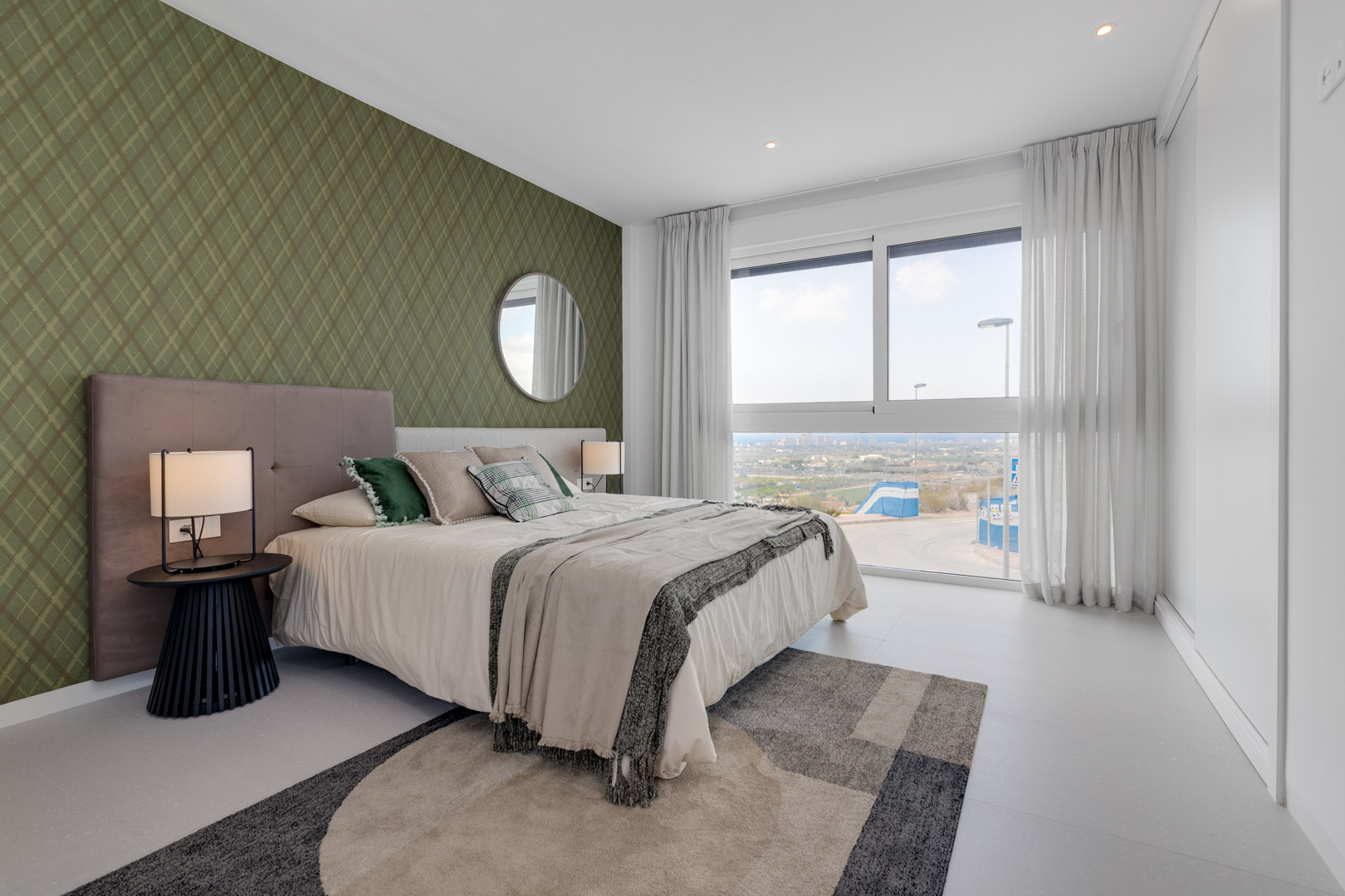 Slaapkamer met groene accentmuur, kamerhoog raam met weids uitzicht en witte inbouwkasten. Voorzien van inbouwspots en een lichte tegelvloer.