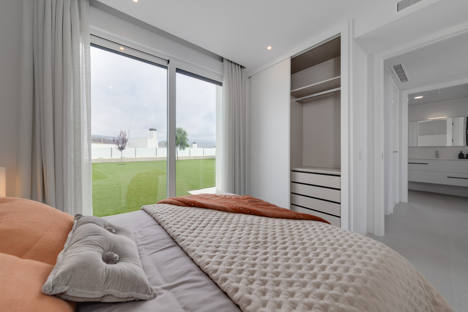 Slaapkamer met inbouwkast, kamerhoge ramen met directe toegang tot de tuin en uitzicht op de en-suite badkamer met zwevend wastafelmeubel.