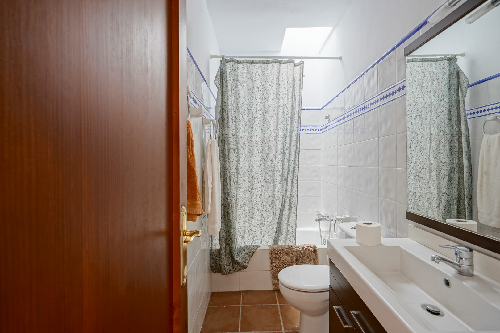 Badkamer met wit-blauwe wandtegels, een modern wastafelmeubel en een ligbad dat wordt verlicht door natuurlijk daglicht via een dakraam.